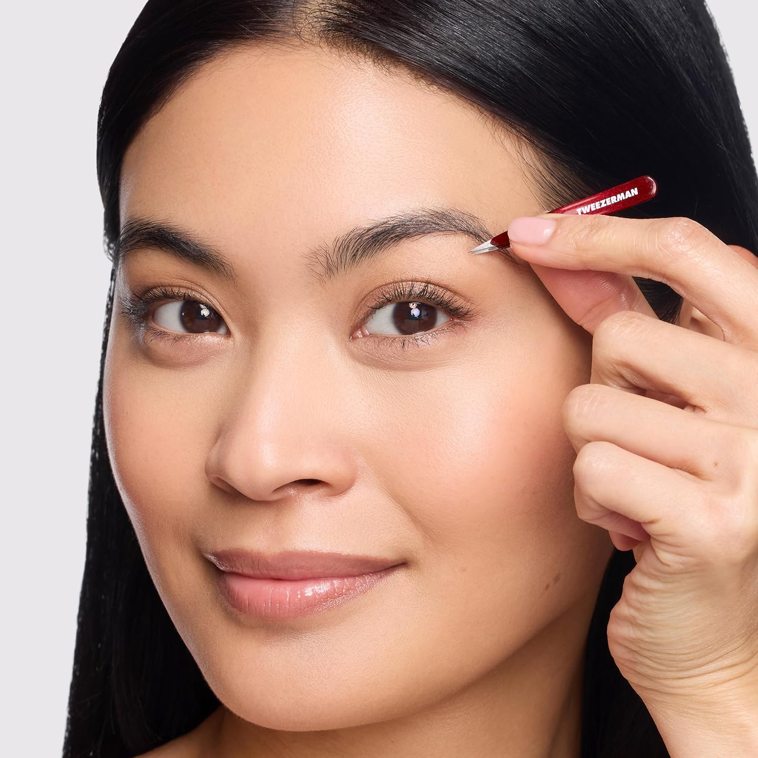 Woman expertly shaping eyebrows with Tweezerman mini tweezer set for precise grooming