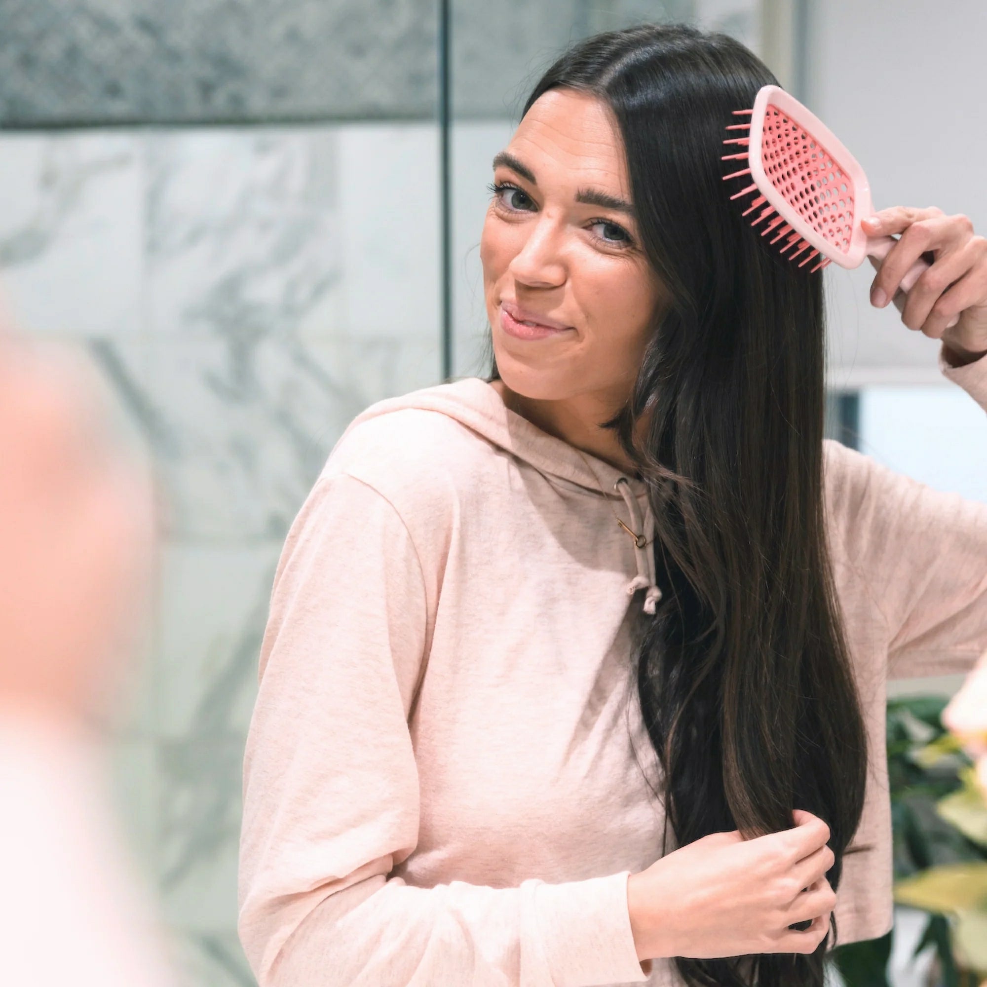 Woman using Unbrush original full sized hair brush to detangle long dark hair in front of mirror