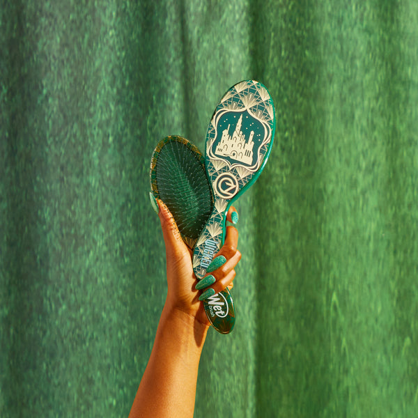 Hand holding Wet Brush Wicked detangling brush with a castle design on green background