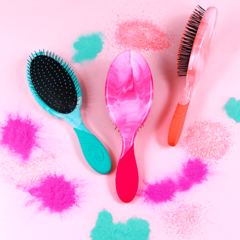 Three colorful Wet Brush Color Shock Pro hairbrushes with marbled handles on pink background