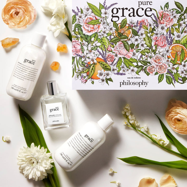 Philosophy Pure Grace gift set with floral illustrated box, eau de toilette, and moisturizing lotions surrounded by flowers