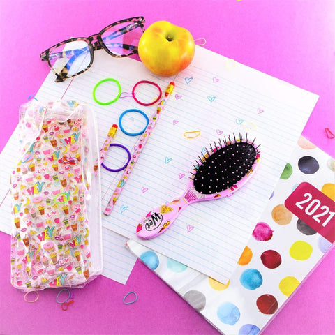 Wet Brush Back to School Detangling Brush Set with pink brush, colorful notebook, pencils, apple, and glasses on pink background
