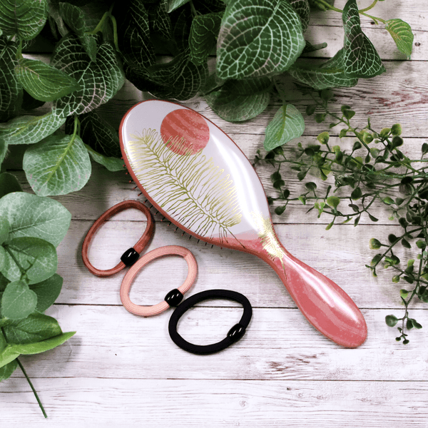 Wet Brush hair styling kit with decorative paddle brush and three elastic hair ties on white wooden surface